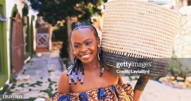 shot of a beautiful young woman wearing traditional african clothing and carrying a basket through a town - african cornrow braids stock pictures, royalty-free photos & images