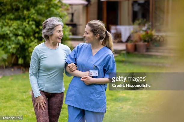 mujer mayor caminando al aire libre con un trabajador de la salud en la comunidad de jubilados - geriatría fotografías e imágenes de stock
