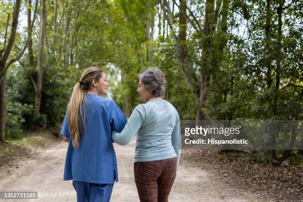 home caregiver walking with a senior woman outdoors - emotional support stock pictures, royalty-free photos & images