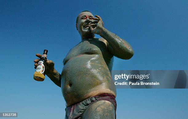 Haim Abisdris of Jerusalem enjoys a beer and a cigarette while the mud from the Dead Sea dries on his body August 24, 2002 at Siesta Beach, Israel....