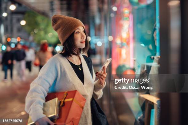 young woman using smartphone while shopping christmas gifts - woman with gift stock pictures, royalty-free photos & images