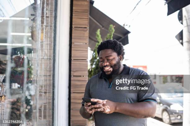 mann benutzt ein mobiltelefon neben einem schaufenster - chubby man shopping stock-fotos und bilder