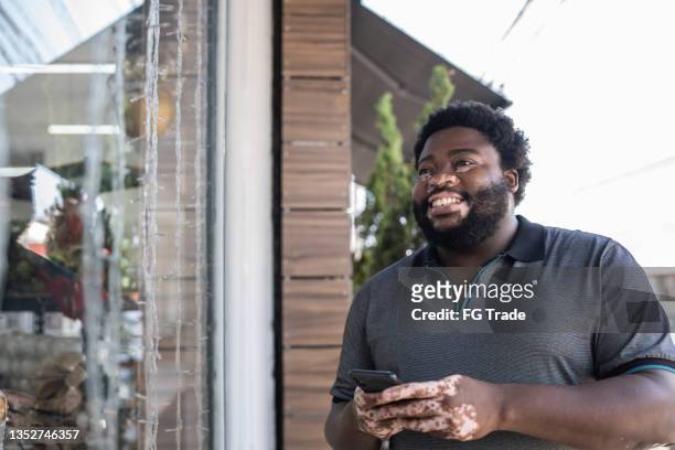 man using a mobile phone beside a store window - chubby man shopping stock pictures, royalty-free photos & images