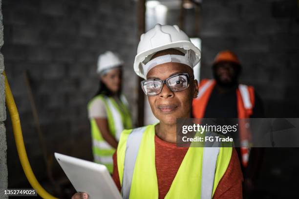 portrait of a female engineer using digital tablet with coworkers on the background in a construction site - stereotypically working class stock pictures, royalty-free photos & images