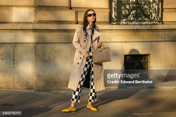Gabriella Berdugo wears a beige trench long coat from Trench London, a black and white checkered print top from Zara, matching high waist pants from...