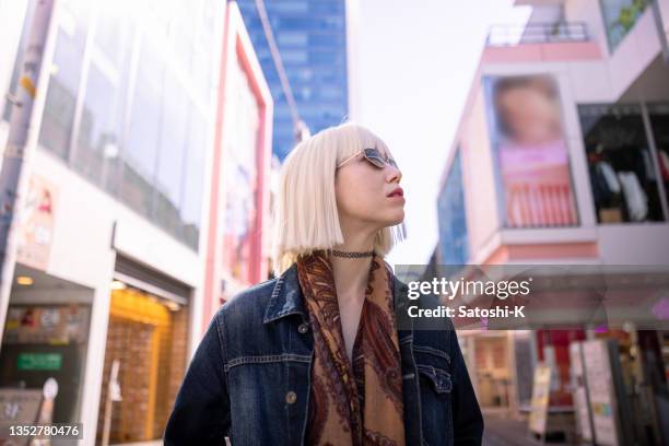 junge frau mit platinblonden haaren und sonnenbrille, die in der pinken einkaufsstraße spazieren geht - frau blond perücke stock-fotos und bilder