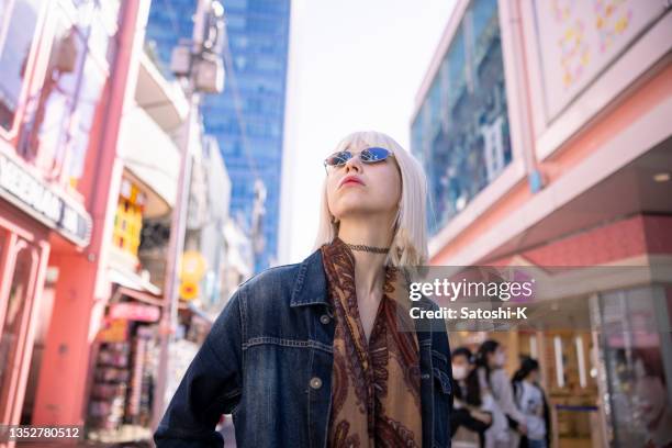 junge frau mit platinblonden haaren und sonnenbrille, die in der pinken einkaufsstraße spazieren geht - shibuya stock-fotos und bilder