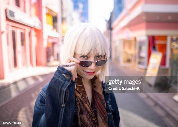 junge frau mit platinblonden haaren und sonnenbrille, die in der pinken einkaufsstraße in die kamera schaut - frau blond perücke stock-fotos und bilder