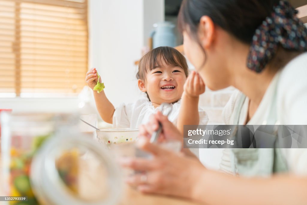 Mother and her small daughter enjoying eating salad and drinking smoothie at home