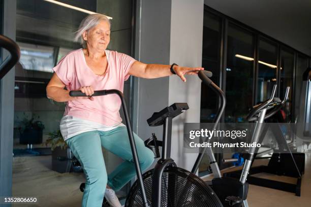senior woman doing exercise in a gym - happy caucasian woman on elliptical trainer at gym stock pictures, royalty-free photos & images
