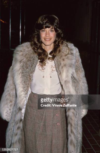 American singer and actress Barbi Benton wearing a fur coat over a white blouse and a grey tweed skirt, circa 1985.