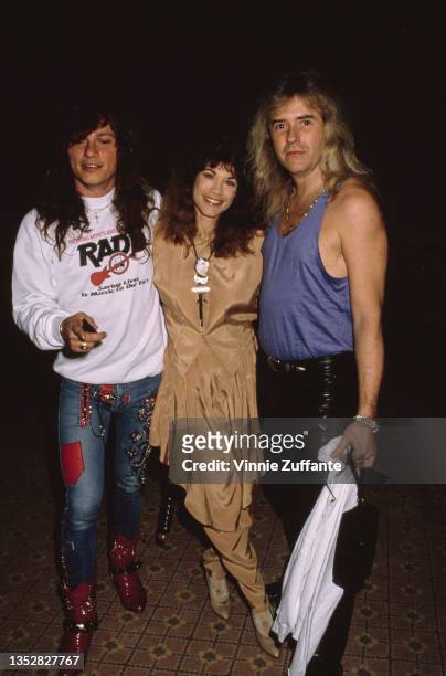 American singer and actress Barbi Benton, wearing a champagne-coloured outfit with matching harem pants, poses with two men, attends an event, circa...