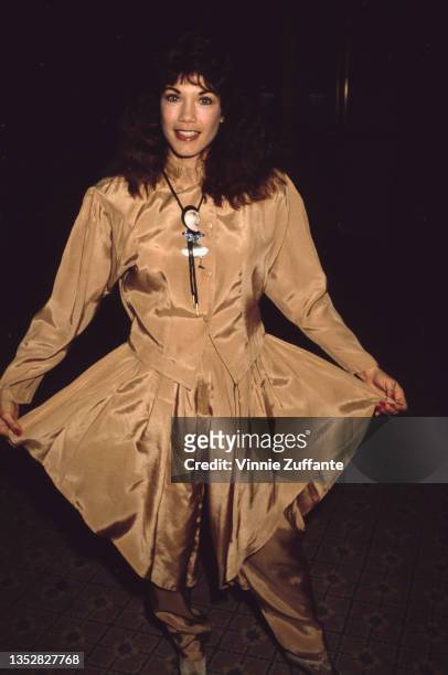 American singer and actress Barbi Benton, wearing a champagne-coloured outfit with matching harem pants, attends an event, circa 1985.