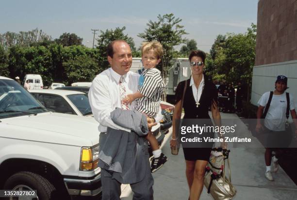 American former professional baseball player Johnny Bench carrying his jacket on one arm and a child on the other, with a woman in a parking lot,...