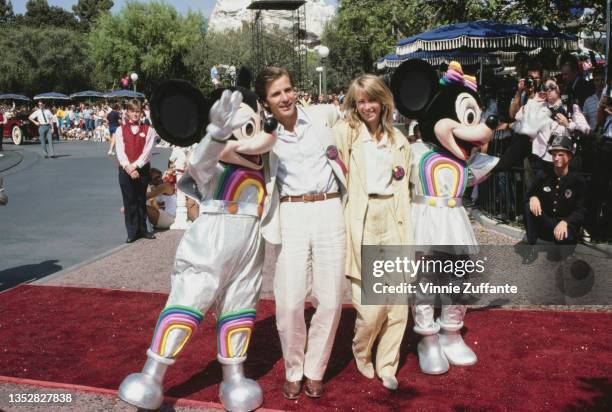 American actor Dirk Benedict, wearing a white suit and white shirt, with his arm around his wife, American actress Toni Hudson, wearing a yellow suit...