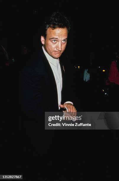 American actor and comedian Jim Belushi, wearing a black suit with a white shirt, attends an event, circa 1990.