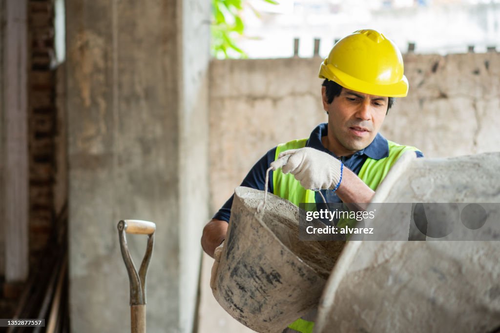 Construction worker adding cement in the concrete mixer at a building site