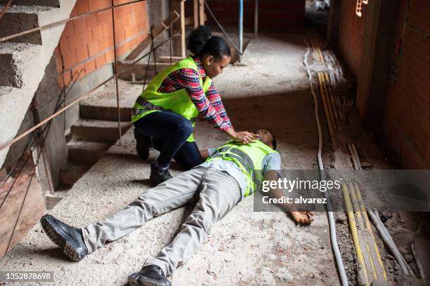 woman trying to revive an unconscious colleague after accident at construction site - woman collapsing stock pictures, royalty-free photos & images