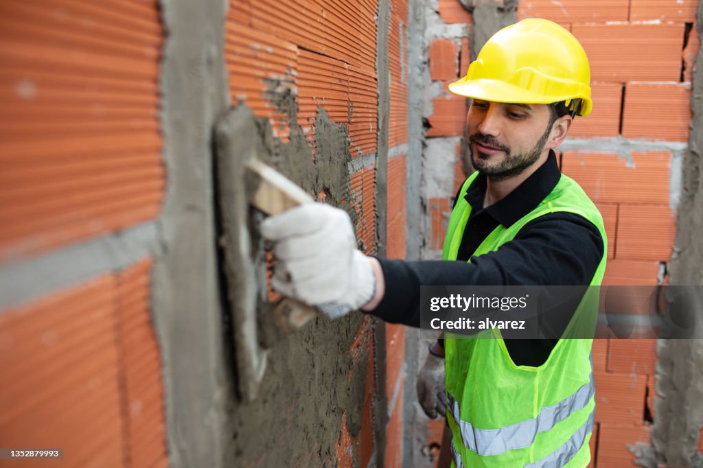 Mason worker plastering cement on brick wall