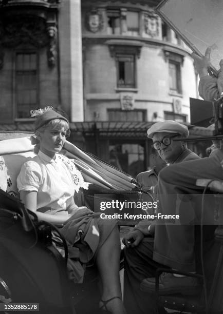 Brigitte Auber et Julien Duvivier à bord d'une calèche lors du tournage du film 'Sous le ciel de Paris', en août 1950.