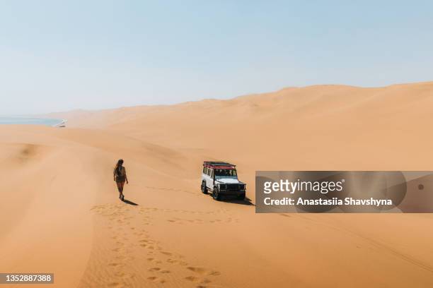 woman traveler enjoying a day at the sand dunes by the sea with 4x4 car in namibia - walvis bay stock pictures, royalty-free photos & images