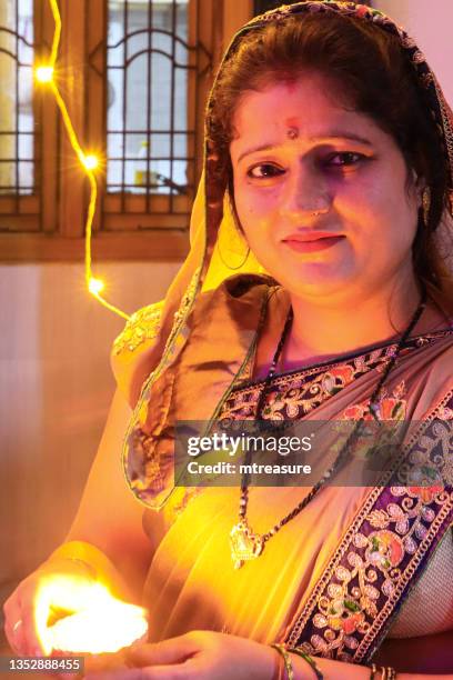 image of indian, hindu woman wearing traditional sari, looking at camera whilst holding a lit diya (oil lamp) flickering flame, diwali festival of lights celebration - diya oil lamp stockfoto's en -beelden