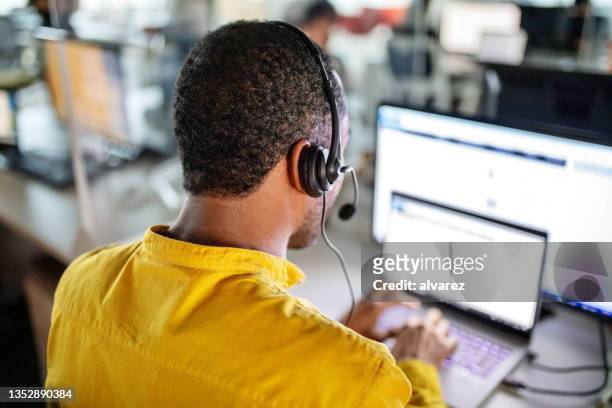 mann mit headset sitzt am schreibtisch und arbeitet an einem laptop - boss over shoulder stock-fotos und bilder