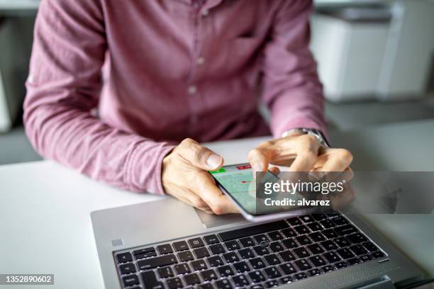 primer plano de un hombre de negocios sentado en su escritorio y usando una aplicación de navegación en su teléfono celular - ampliar fotografías e imágenes de stock