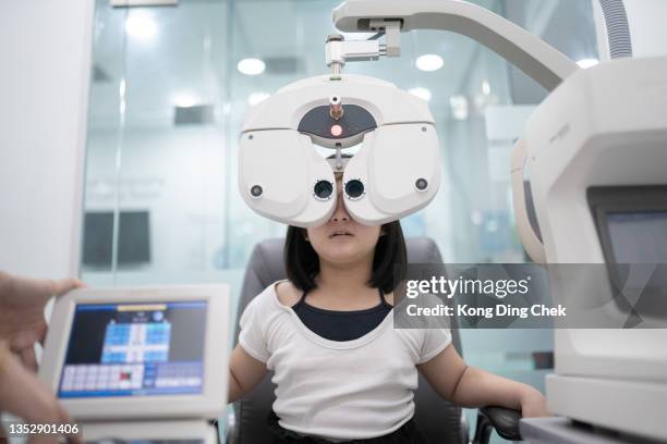 une fille chinoise asiatique assise sur une chaise en train de faire un test oculaire sur phoropter numérique dans une clinique d’ophtalmologie - réfracteur photos et images de collection