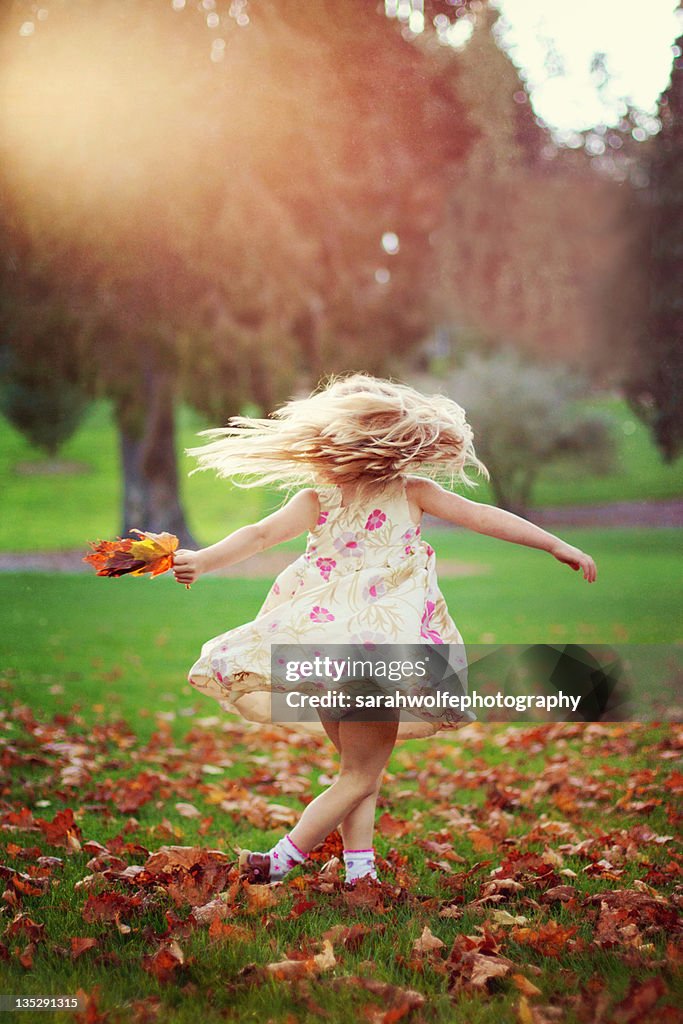 Young girl twirling in autumn leaves