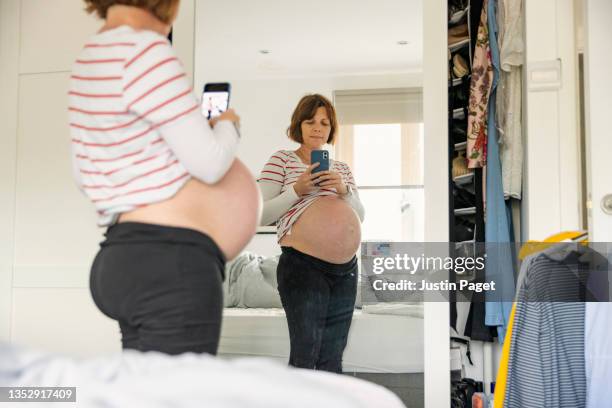 mature pregnant woman taking a selfie in her bedroom mirror - selfie-in-mirror foto e immagini stock