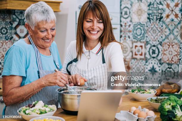 mother and daughter watching recipe on digital tablet while cooking lunch in modern kitchen. - cookery class stock pictures, royalty-free photos & images