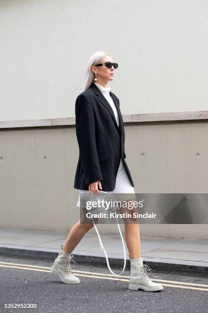 Daria Suchenek wears a Topshop top, vintage jacket, Jacquemus earrings and bag, Staccato boots, H&M shorts and Balenciaga sunglasses during London...