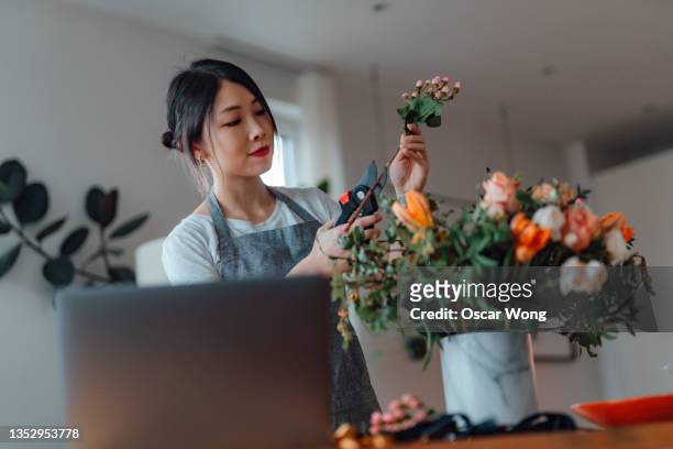 young woman arranging flowers while doing online workshop - floral decoration stock pictures, royalty-free photos & images