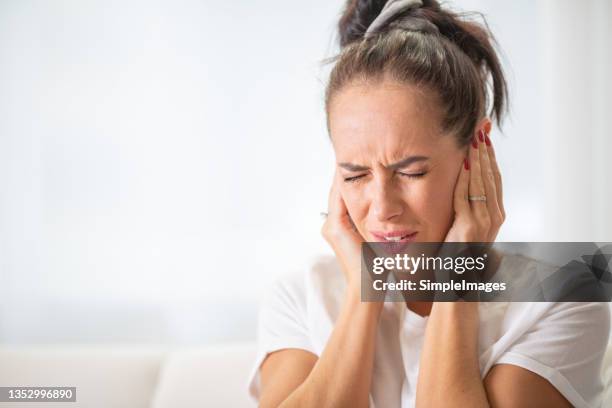 woman closes hear ears with hands due to noise or ache in the ear or head frowning from the unpleasant experience. - ear stockfoto's en -beelden