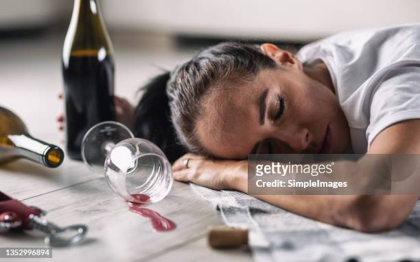 drunk woman fell asleep on the floor at home with glass of red wine spilled next to her. - woman binge drinking stock pictures, royalty-free photos & images