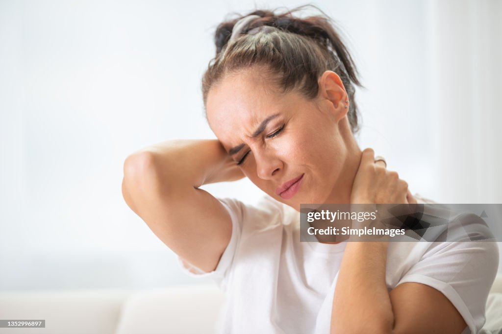 Woman with pain in the nech holding it with both arms with painful expression on her face.