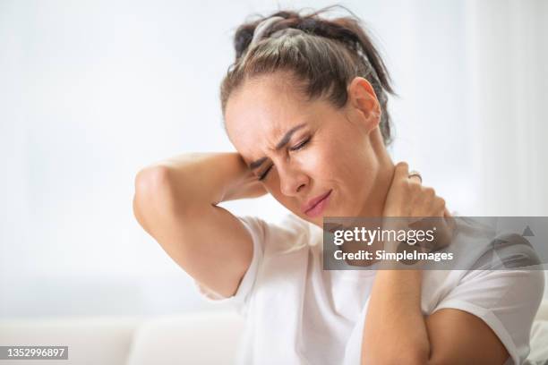 woman with pain in the nech holding it with both arms with painful expression on her face. - inflamação imagens e fotografias de stock