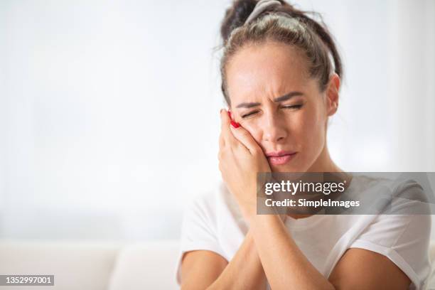 toothache experienced by a young woman holding her cheek with both hands. - pain face stock-fotos und bilder