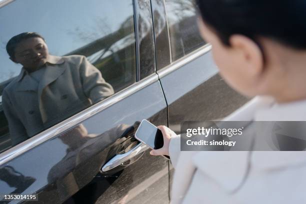 asian business lady unlock her car with smartphone - auto tür offen stock-fotos und bilder