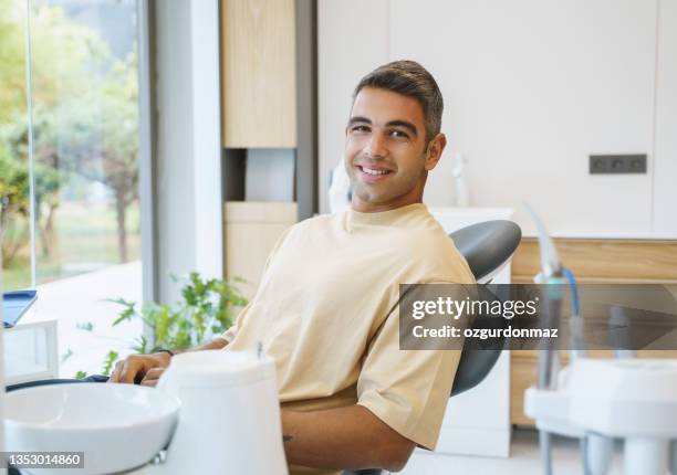 portrait of happy young man sitting in a dentist’s chair - tandartsstoel stockfoto's en -beelden