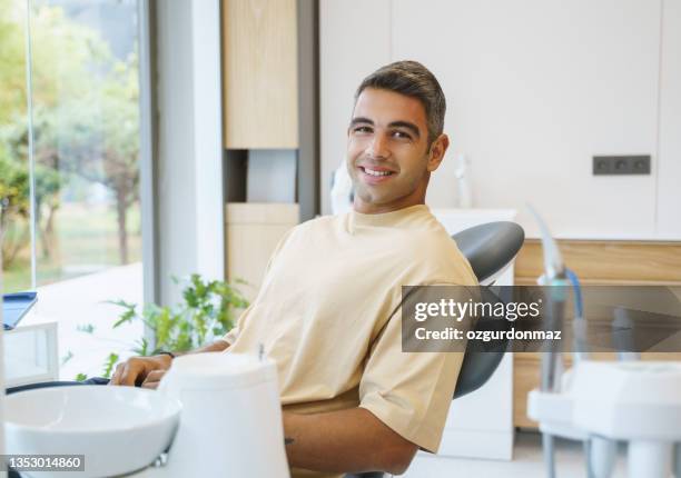 portrait of happy young man sitting in a dentist’s chair - dentists chair stock pictures, royalty-free photos & images