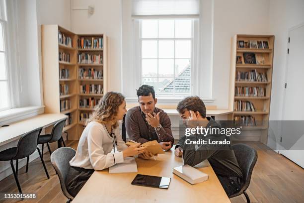 three university students working together in a public library - onderwijsinstituten en organisaties stockfoto's en -beelden