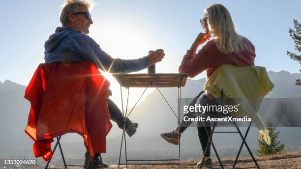 couple enjoy hot beverage on a mountain ridge at sunset - canmore stock pictures, royalty-free photos & images