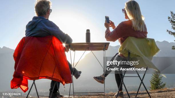 couple enjoy hot beverage on a mountain ridge at sunset - canmore stock pictures, royalty-free photos & images