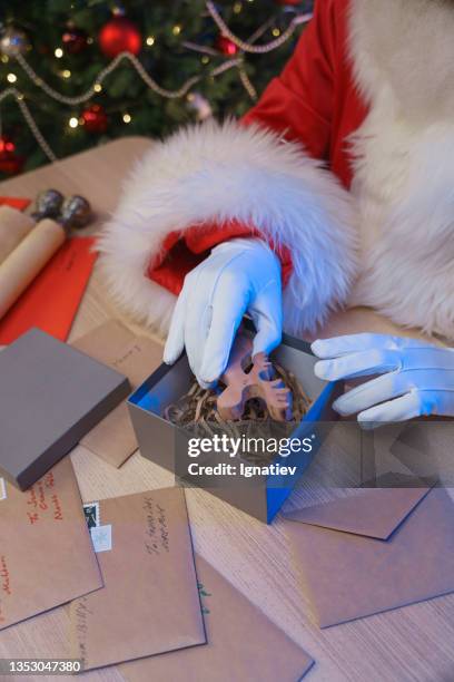 der weihnachtsmann in weißen handschuhen legt ein elchspielzeug in eine geschenkbox. - secret santa stock-fotos und bilder