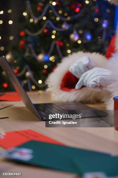 nahaufnahme der hände des weihnachtsmanns in weißen handschuhen, die text auf einer laptop-tastatur vor dem hintergrund eines weihnachtsbaums tippen. - santa close up stock-fotos und bilder
