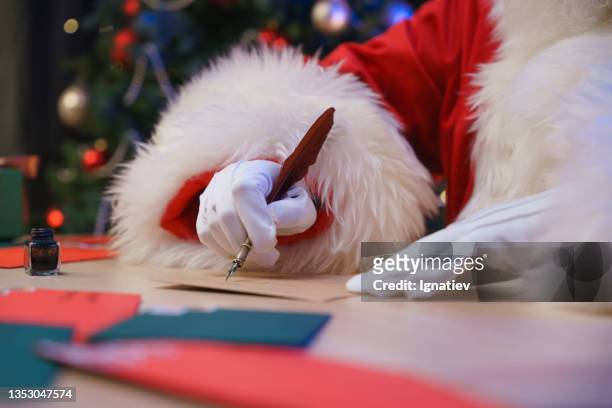 der weihnachtsmann sitzt neben einem weihnachtsbaum und schreibt einen brief - secret santa stock-fotos und bilder