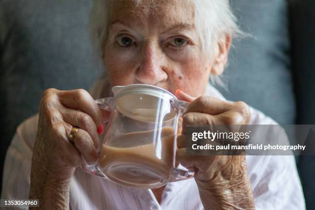 senior lady drinking tea from beaker - rheuma stock-fotos und bilder