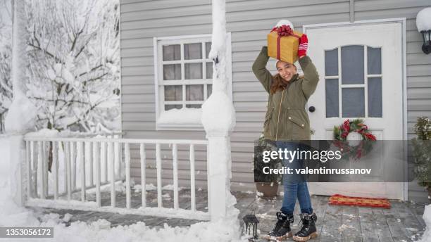 portrait of a young teenage girl smiling in front of a snowy porch, holding a christmas gift above her head - above the threshold stockfoto's en -beelden